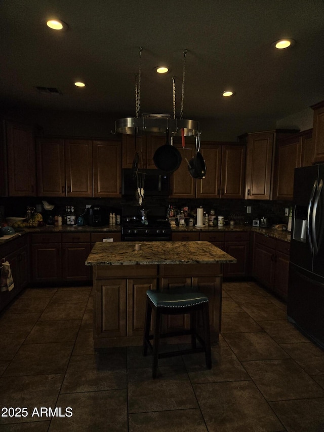 kitchen with black appliances, stone countertops, a kitchen island, and recessed lighting