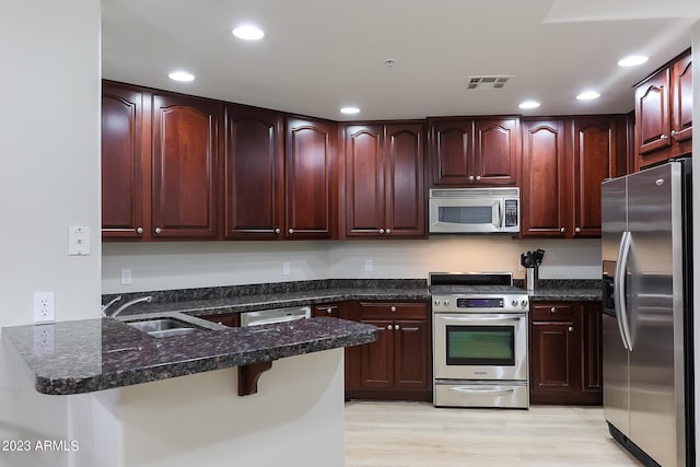 kitchen featuring sink, a breakfast bar area, dark stone counters, stainless steel appliances, and light hardwood / wood-style floors