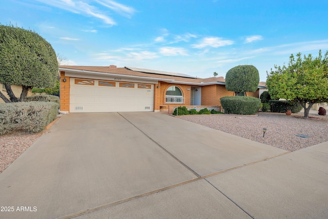 single story home with a garage, solar panels, brick siding, and driveway