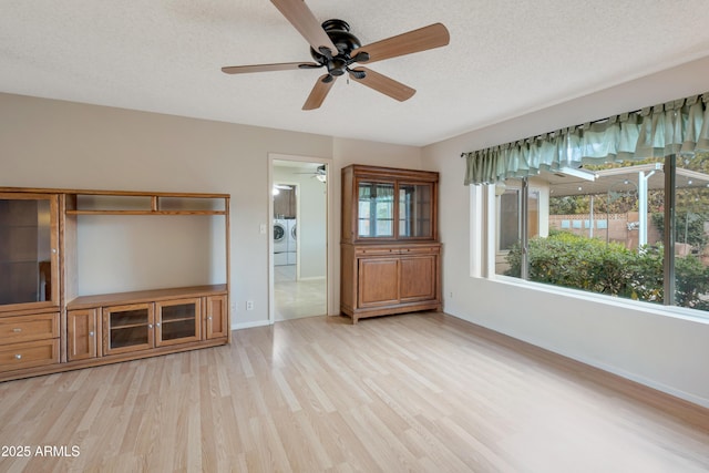 unfurnished living room featuring washer and clothes dryer, a textured ceiling, baseboards, and wood finished floors