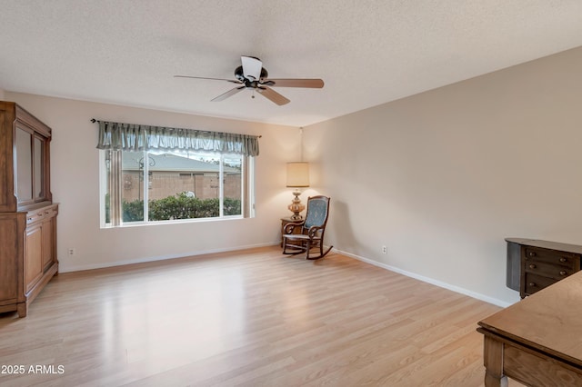 living area with a ceiling fan, light wood-type flooring, a textured ceiling, and baseboards