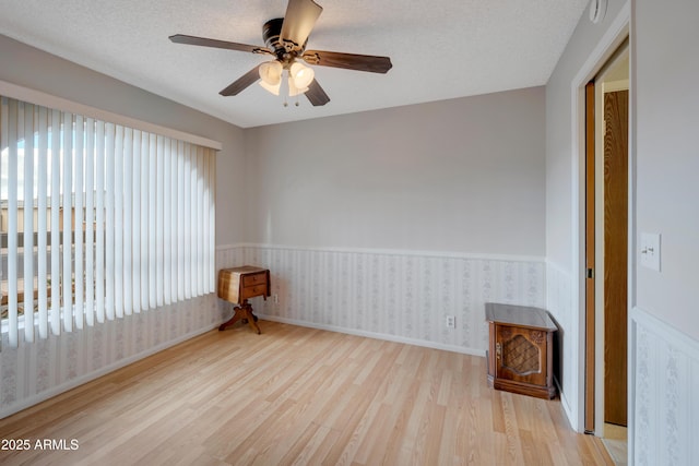 spare room with a wainscoted wall, ceiling fan, a textured ceiling, wood finished floors, and wallpapered walls