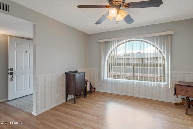 living area featuring a wainscoted wall, a textured ceiling, visible vents, and wallpapered walls