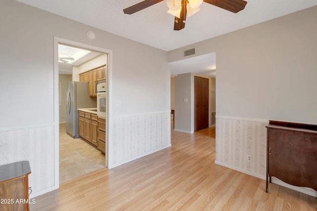 unfurnished room featuring baseboards, light wood finished floors, visible vents, and a ceiling fan