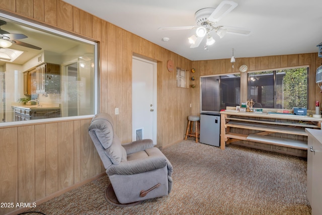 sitting room with ceiling fan, carpet floors, wood walls, and visible vents