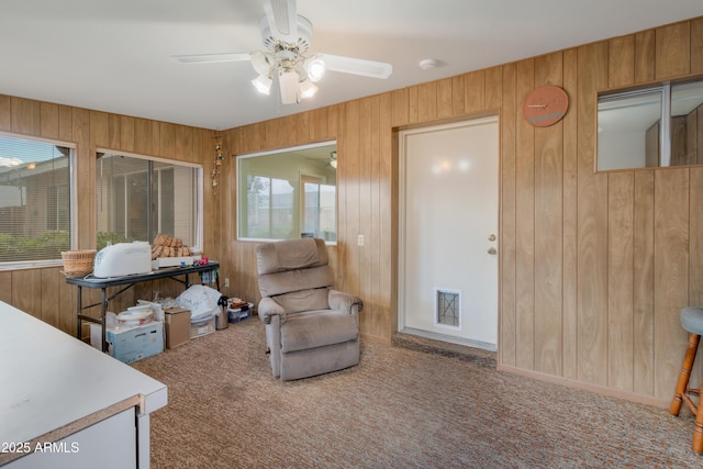 living area with ceiling fan, carpet floors, plenty of natural light, and wooden walls