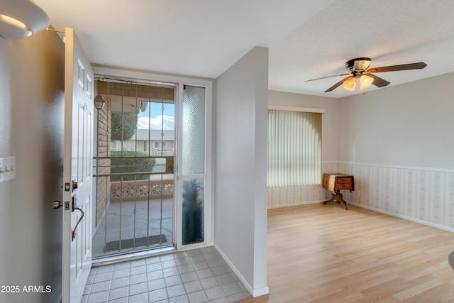 foyer entrance with a textured ceiling, wood finished floors, a ceiling fan, baseboards, and wainscoting