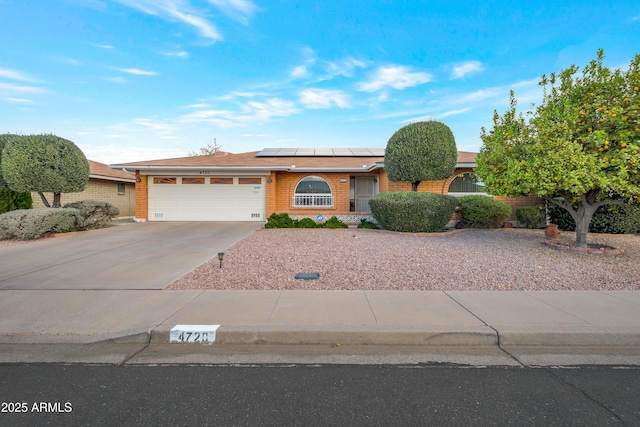 ranch-style house featuring an attached garage, solar panels, concrete driveway, and brick siding