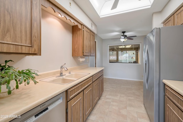 kitchen with a skylight, a ceiling fan, appliances with stainless steel finishes, light countertops, and a sink