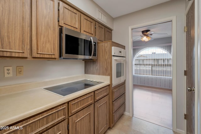 kitchen with a ceiling fan, stainless steel microwave, oven, black electric stovetop, and light countertops