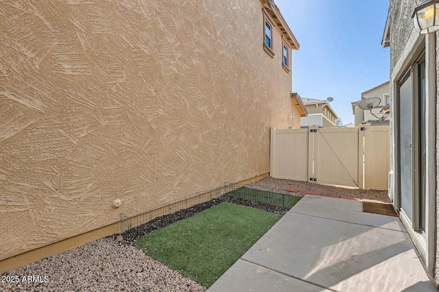 view of side of property with a gate, fence, a patio, and stucco siding