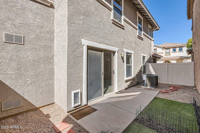 property entrance featuring a patio, central air condition unit, fence, visible vents, and stucco siding