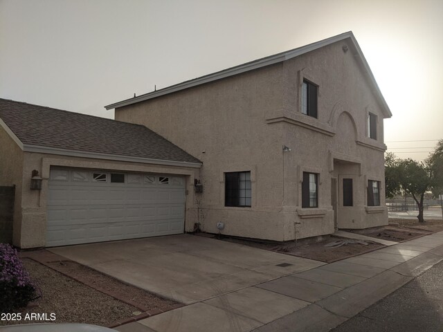 view of side of property featuring concrete driveway, a shingled roof, an attached garage, and stucco siding