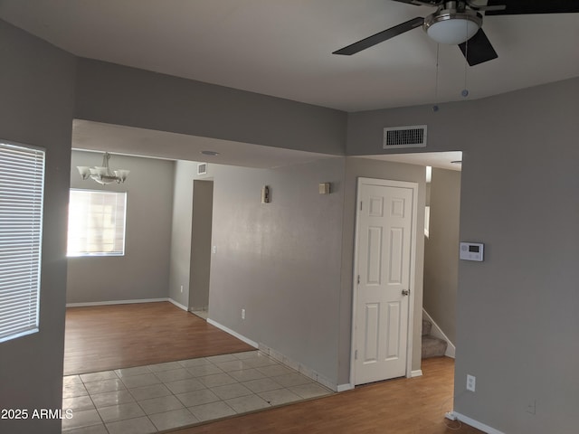 spare room with stairs, visible vents, wood finished floors, and ceiling fan with notable chandelier