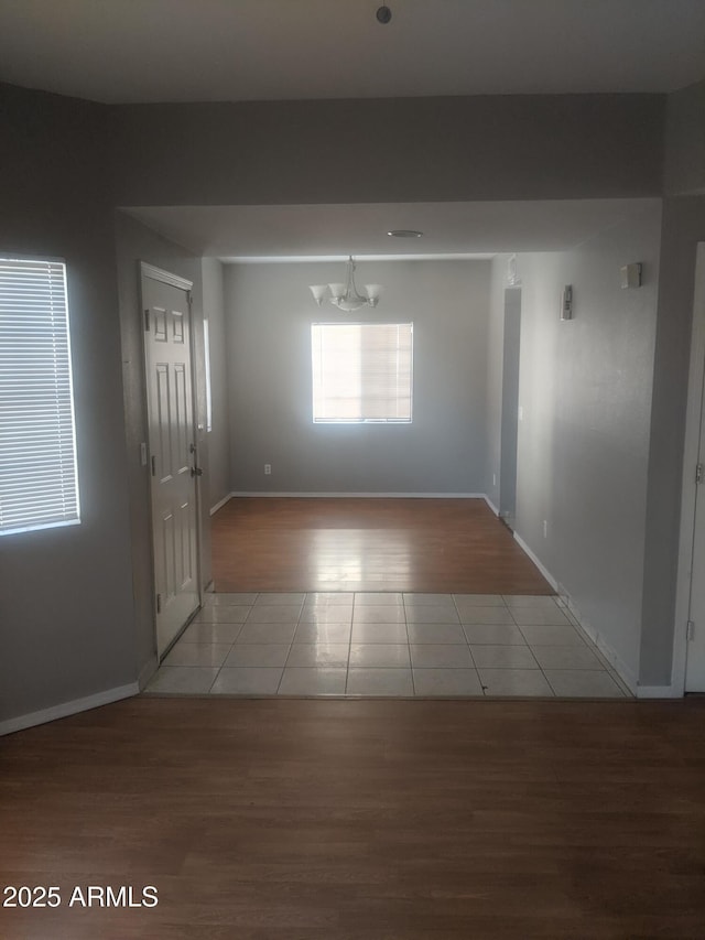 tiled empty room featuring baseboards and an inviting chandelier