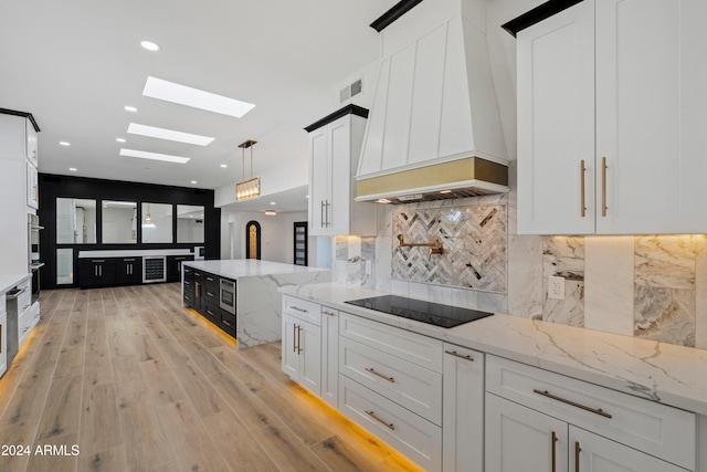 kitchen featuring premium range hood, appliances with stainless steel finishes, decorative light fixtures, white cabinets, and light stone countertops