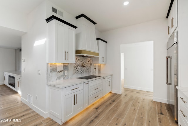 kitchen featuring high end fridge, light stone counters, custom exhaust hood, and white cabinets