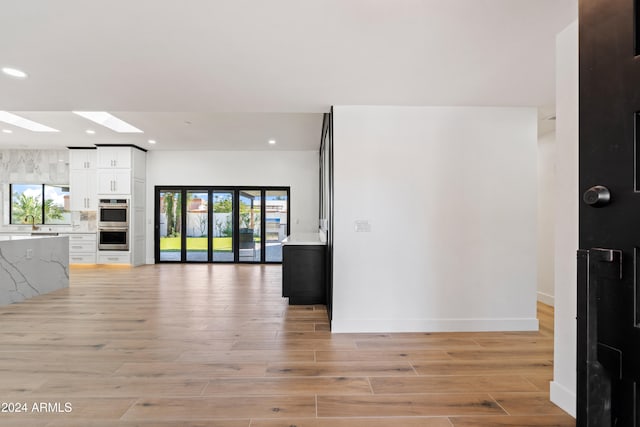 kitchen with white cabinetry, a skylight, light hardwood / wood-style floors, and double oven