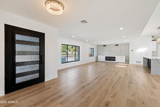 unfurnished living room with a chandelier and light wood-type flooring