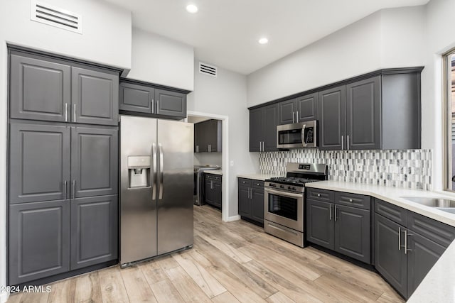 kitchen with appliances with stainless steel finishes, a towering ceiling, backsplash, sink, and light hardwood / wood-style flooring