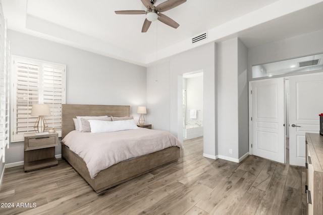 bedroom with connected bathroom, light hardwood / wood-style floors, a raised ceiling, and ceiling fan