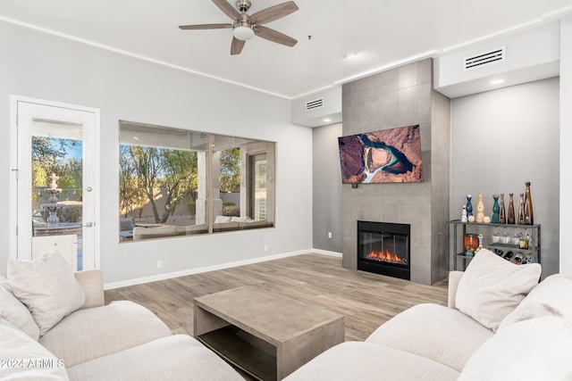 living room with ceiling fan, light hardwood / wood-style flooring, and a tiled fireplace