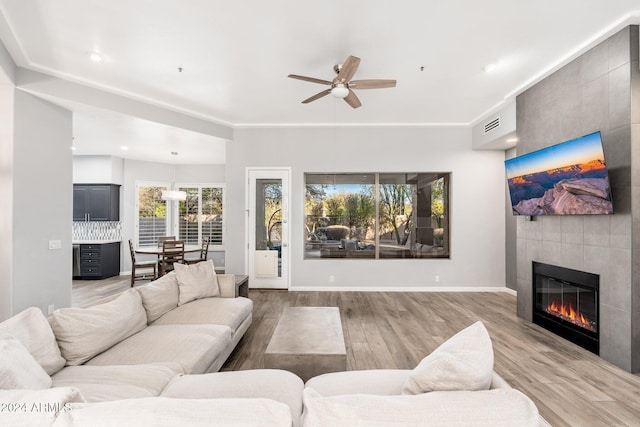 living room with ceiling fan, light wood-type flooring, and a tiled fireplace