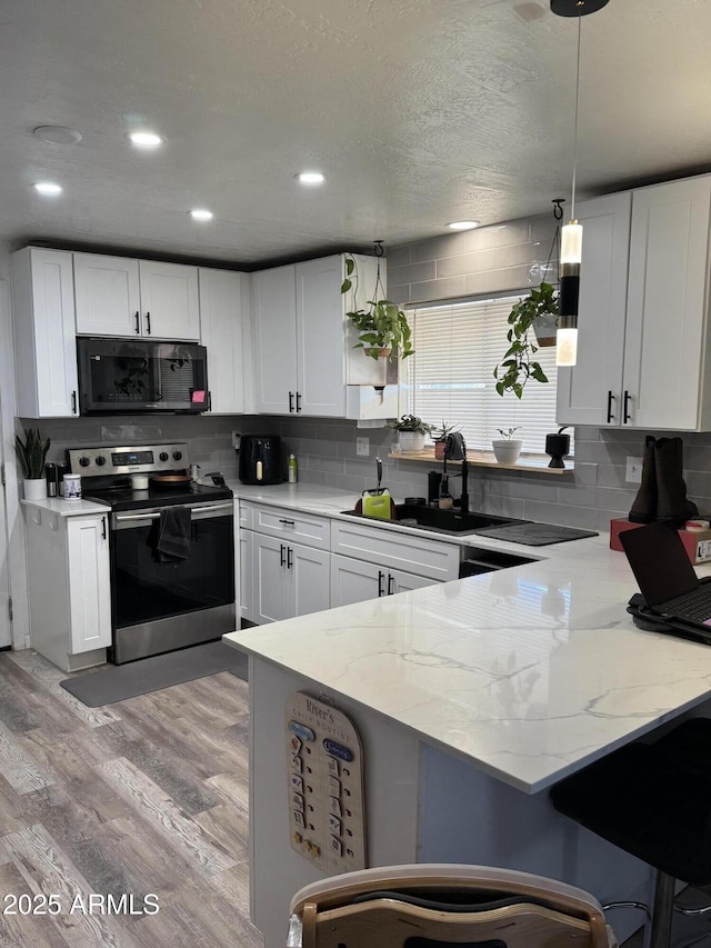 1705 S Cedar Dr, Apache Junction, AZ 85120 - kitchen with black microwave, electric range, a peninsula, a kitchen bar, and light wood-style floors