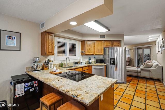 kitchen with a kitchen bar, sink, light stone counters, appliances with stainless steel finishes, and kitchen peninsula