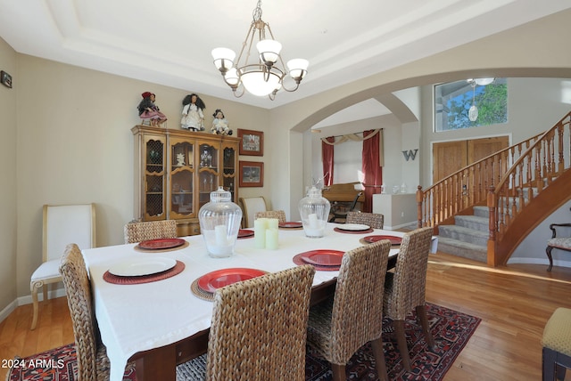 dining area with a notable chandelier, a raised ceiling, and light wood-type flooring