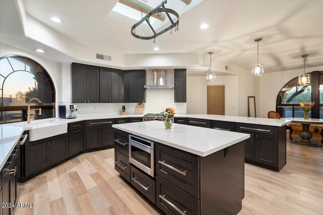 kitchen featuring hanging light fixtures, a center island, stainless steel microwave, sink, and wall chimney range hood