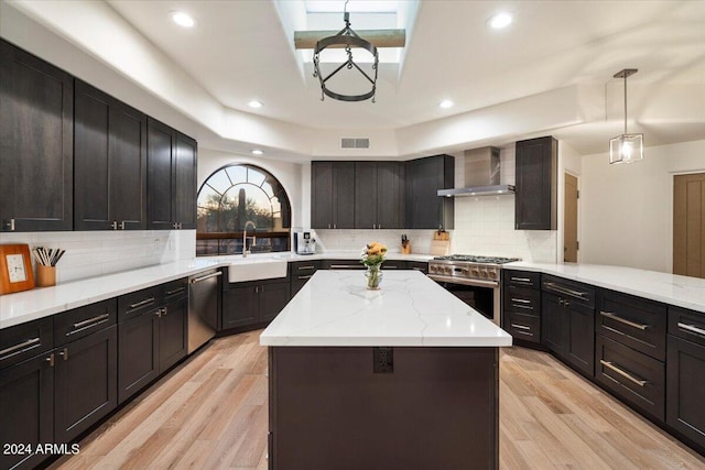 kitchen featuring wall chimney exhaust hood, a kitchen island, light wood-type flooring, backsplash, and appliances with stainless steel finishes