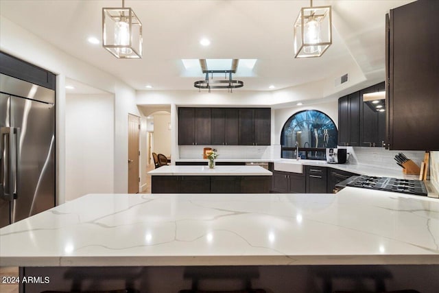 kitchen with decorative light fixtures, decorative backsplash, light stone countertops, a kitchen island, and high end refrigerator