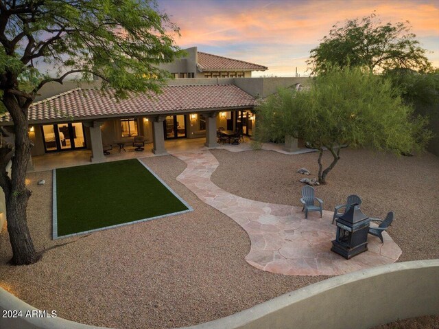 back house at dusk featuring a patio and an outdoor fire pit