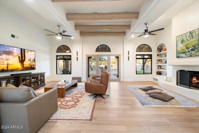 living room featuring light hardwood / wood-style floors, beamed ceiling, ceiling fan, french doors, and built in shelves