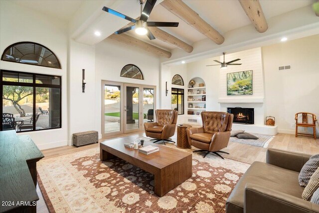 living room featuring beamed ceiling, ceiling fan, a fireplace, light hardwood / wood-style flooring, and built in features