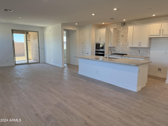 kitchen with white cabinetry, stainless steel microwave, light stone countertops, oven, and a kitchen island with sink