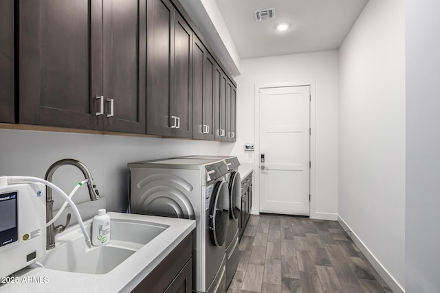 clothes washing area with washing machine and dryer, wood finished floors, visible vents, a sink, and cabinet space