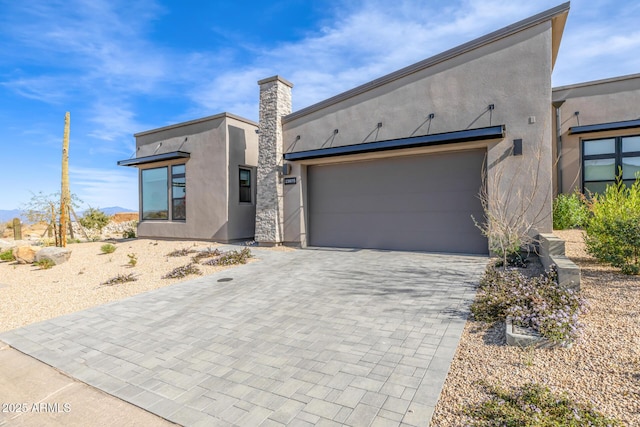 contemporary home with decorative driveway, an attached garage, and stucco siding