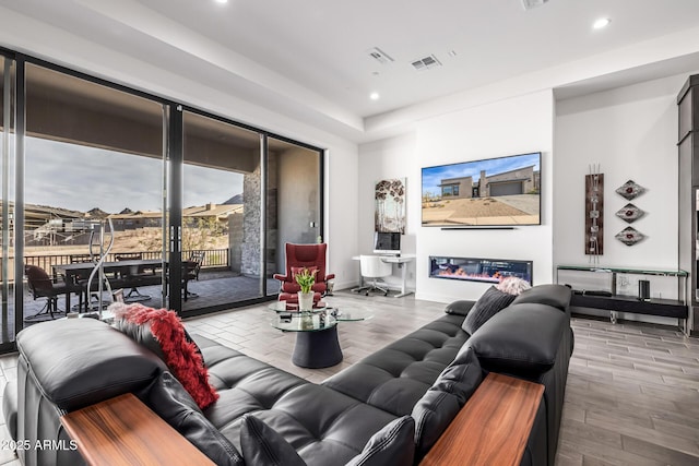 living area with recessed lighting, visible vents, wood finished floors, and a glass covered fireplace