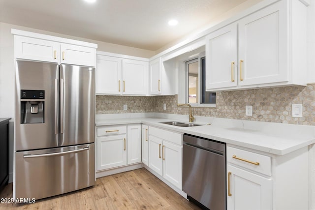 kitchen featuring white cabinetry, sink, backsplash, stainless steel appliances, and light hardwood / wood-style flooring