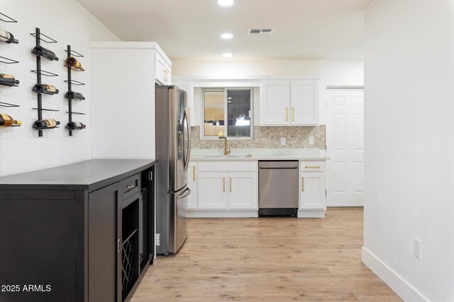 kitchen featuring sink, white cabinetry, appliances with stainless steel finishes, light hardwood / wood-style floors, and decorative backsplash