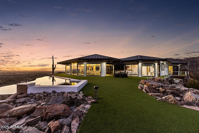 back house at dusk featuring a water view and a yard