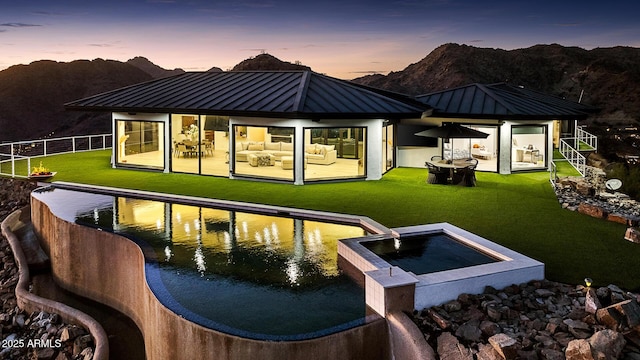 back house at dusk featuring a mountain view and a lawn