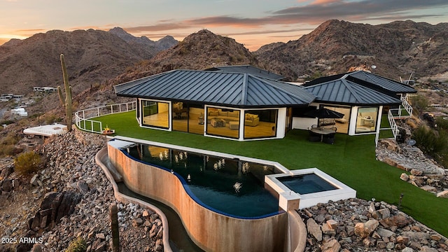 back house at dusk with an in ground hot tub and a mountain view