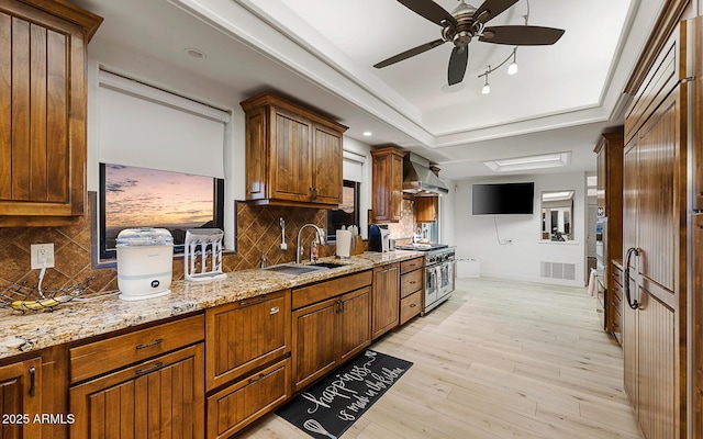 kitchen with sink, range with two ovens, a raised ceiling, light stone countertops, and light hardwood / wood-style flooring