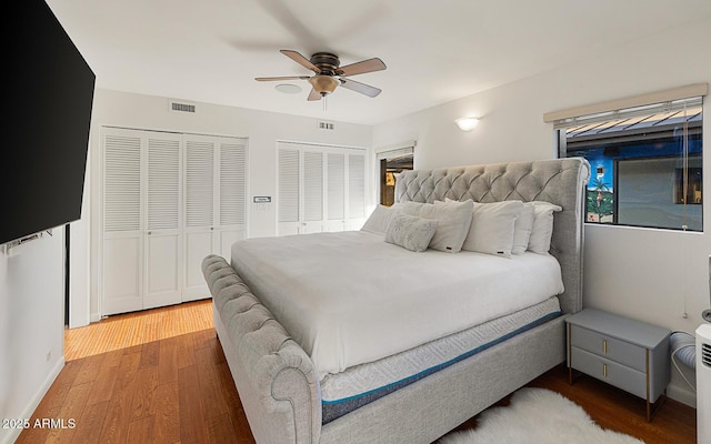 bedroom with two closets, wood-type flooring, and ceiling fan