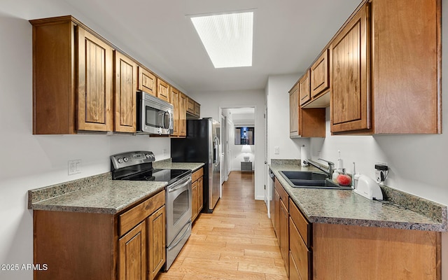 kitchen with stainless steel appliances, sink, light hardwood / wood-style floors, and a skylight