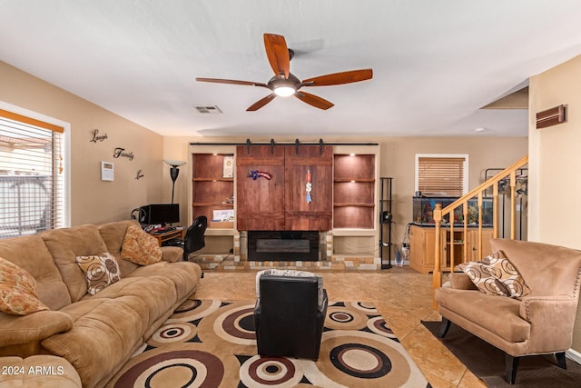 tiled living room with a ceiling fan, a glass covered fireplace, visible vents, and stairway