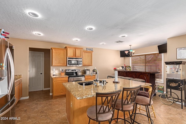 kitchen featuring light stone counters, a breakfast bar area, stainless steel appliances, visible vents, and a sink